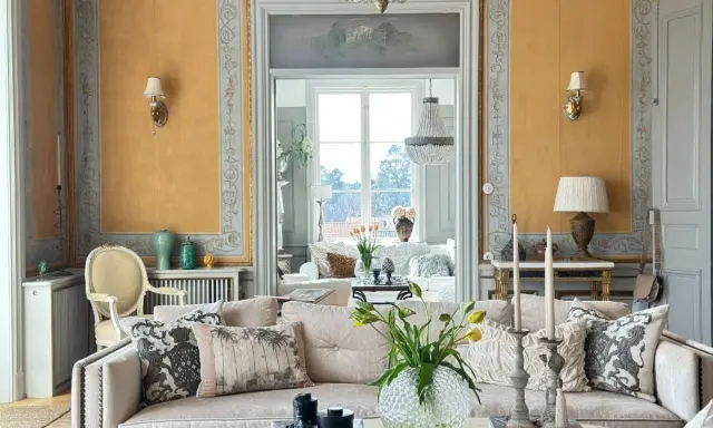Ett elegant vardagsrum med fransk inredningsstil. Gyllene väggar, kristallkrona och antika möbler skapar en lyxig atmosfär.