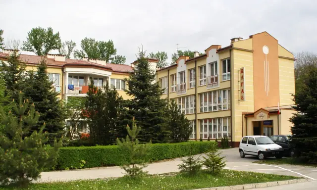 Sanatorium Rafał Busko Zdrój, z żółtą fasadą i zielenią wokół, zaprasza na wypoczynek.