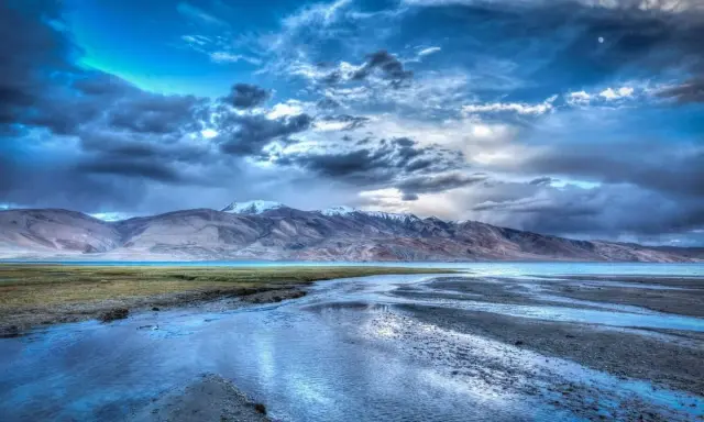 Paesaggio montano con lago e fiume, cielo drammatico con nuvole scure e luna, effetto HDR.
