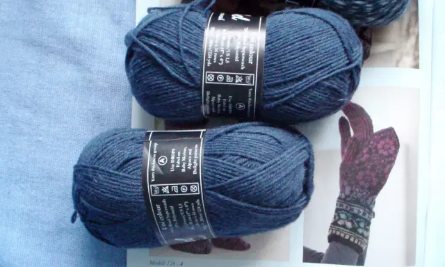 Two balls of dark blue yarn and a knitted glove with a floral pattern.