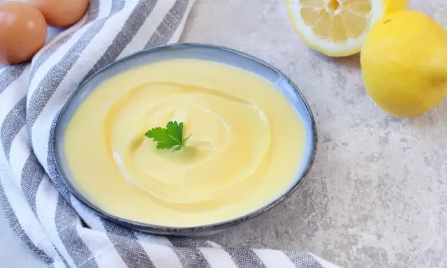 Cremige Joghurt-Mayonnaise mit Zitrone und Petersilie, daneben Eier und Zitronen.