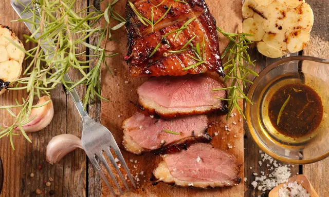 Magret de canard tranché, servi avec une sauce pour magret de canard, romarin, ail rôti et gros sel.