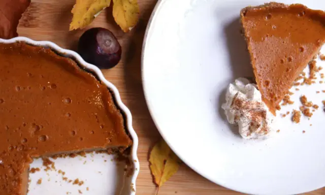 La tarta de calabaza de la abuela, con su relleno cremoso y corteza dorada, lista para ser disfrutada. Una rebanada servida con nata montada y canela.
