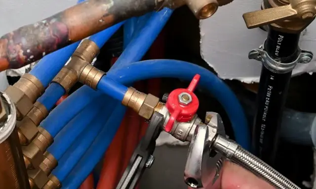 Réglage de la vanne arrivée d'eau maison avec une clé. Tuyaux bleus et rouges, raccords en laiton.