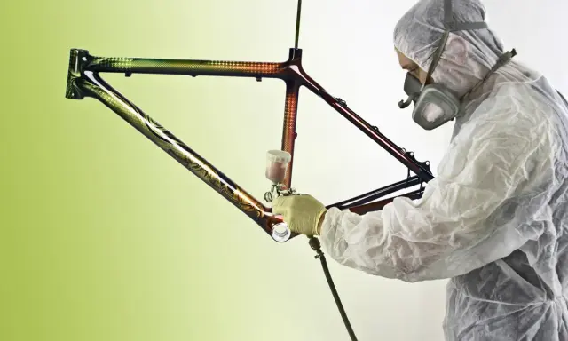 Person in Schutzanzug lackiert kunstvoll einen Rennrad Rahmen mit Spraydose.