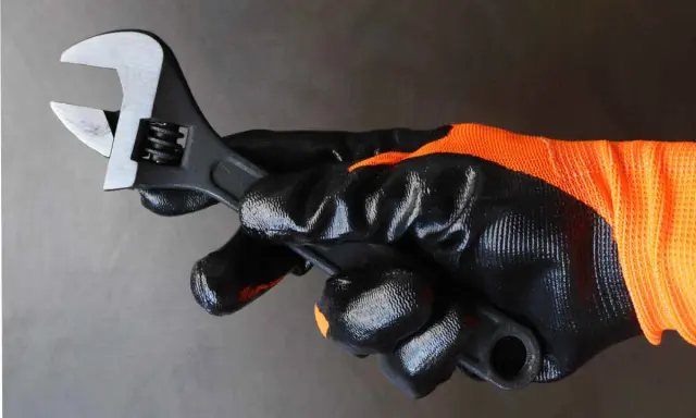 Mano enguantada sujeta llave inglesa ajustable, herramienta esencial para saber para que sirve la llave inglesa al apretar o aflojar tuercas y tornillos.