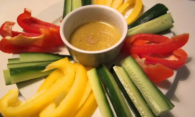 En skål med bagna cauda-sås omgiven av färgglada grönsaksstavar: röd och gul paprika samt gurka.