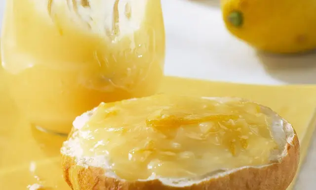 Ein Brötchen mit cremigem Lemon Curd, das ist die Antwort auf die Frage: was ist Lemon Curd. Daneben ein Glas voller dieser gelben Köstlichkeit.
