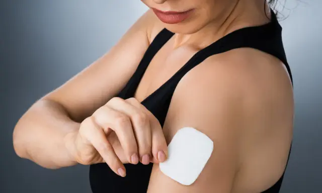 Kobieta przykleja plaster antykoncepcyjny na ramię. Poznaj, jak działają plastry antykoncepcyjne, uwalniając hormony przez skórę.