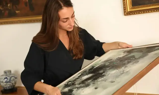 Une femme examine un tableau abstrait, cherchant des indices pour comment estimer un tableau avec signature.