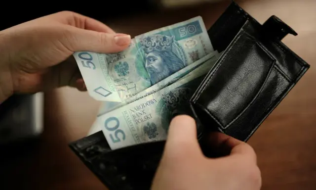 Ręce wkładają polskie banknoty 50 zł do czarnego portfela. To kieszonkowe dla dziecka na drobne wydatki.