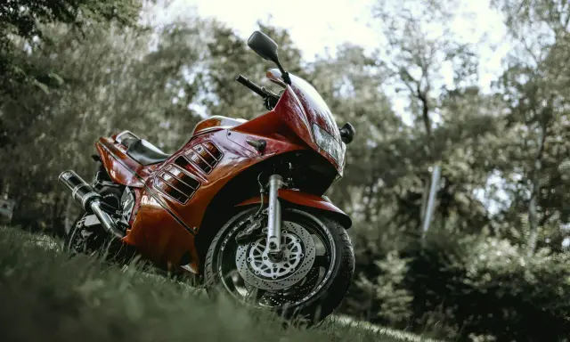 Czerwony motocykl Suzuki RF 900, zaparkowany na trawie wśród drzew. Idealny do sprawdzenia jego danych technicznych.