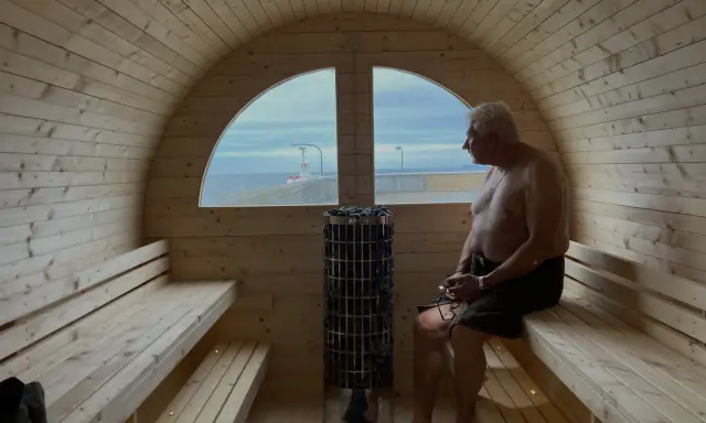 Man njuter av värmen i en bastuflotte i Skåne med utsikt över havet och en fyr.