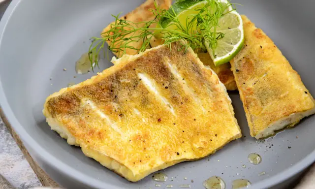 Zanderfilet ohne Haut braten: goldbraune Fischfilets auf grauem Teller, garniert mit Dill und Limettenspalten.