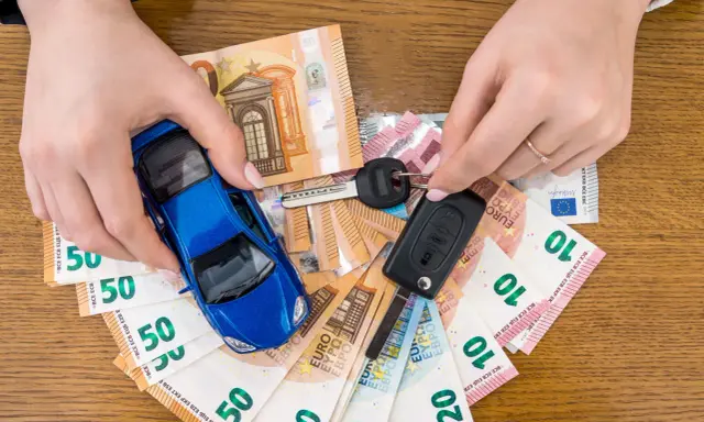 Manos sostienen un coche azul de juguete, llaves y billetes de euro. El coche no arranca, quizás por falta de dinero.