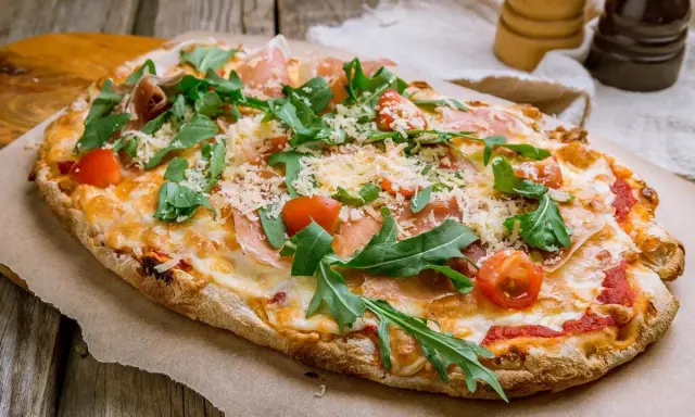 Eine leckere Pinsa belegen mit Schinken, Rucola und Kirschtomaten. Käse und Tomatensauce runden den Genuss ab.