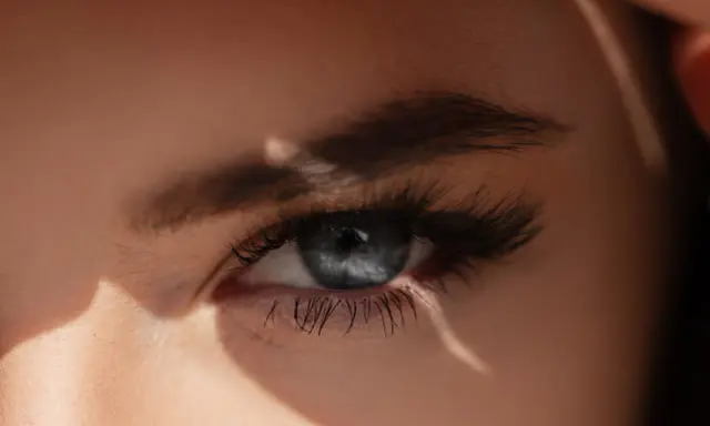 Un œil bleu intense, sublimé par un microblading parfait, capte la lumière du soleil.