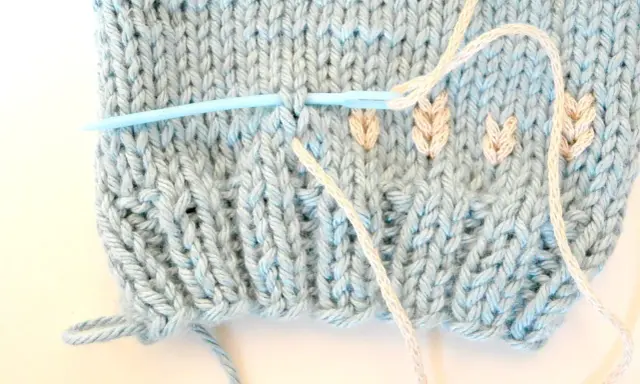 Agujas de punto plumeti dos agujas, creando un delicado diseño de hojas en tejido azul claro.