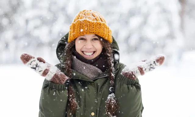 Una chica sonríe felizmente en medio de una nevada, con su gorro naranja y guantes a juego. ¡Bonitas fotos en la nieve!