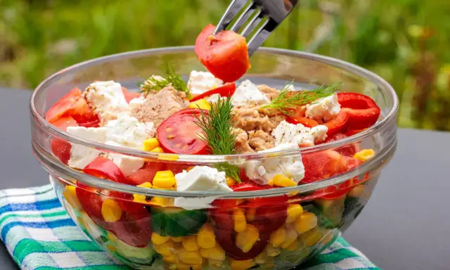 Szybkie i tanie sałatki to idealny pomysł na lekki posiłek. W szklanej misce kolorowa sałatka z pomidorów, ogórka, kukurydzy, papryki, sera feta i tuńczyka.