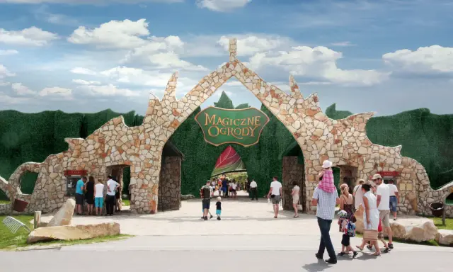 Kamienna brama z napisem "Magiczne Ogrody" zaprasza na niezapomniane atrakcje dla dzieci mazowieckie. Rodziny wchodzą do bajkowego świata.