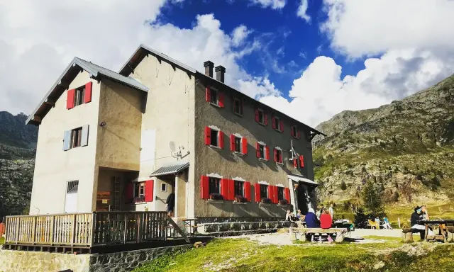 Rifugi raggiungibili in auto a Bergamo: un edificio con persiane rosse in montagna, con persone sedute fuori.