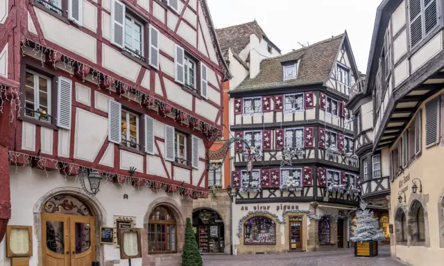 Fachwerkhäuser mit roten und weißen Fassaden in der Colmar Altstadt, geschmückt mit Lichterketten und Weihnachtsdekoration.