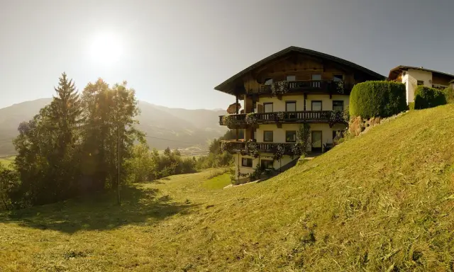 Haus im Alpenvorland mit traditioneller Architektur und Balkonen, umgeben von grünen Wiesen und Bergen.