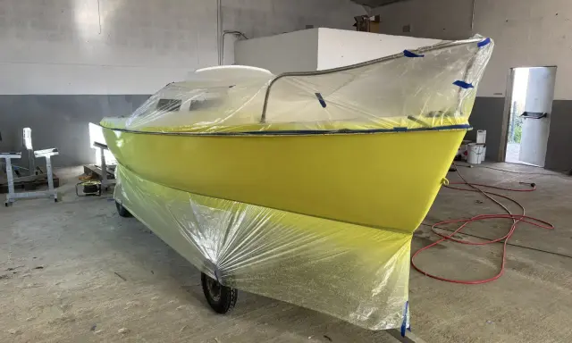 Un bateau jaune est bâché pour le repeindre. Il est sur une remorque dans un atelier.