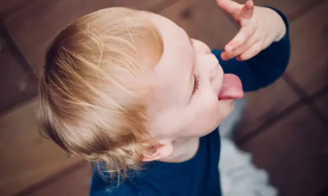 Małe dziecko nie słucha w przedszkolu, wyciąga język i bawi się jedzeniem.