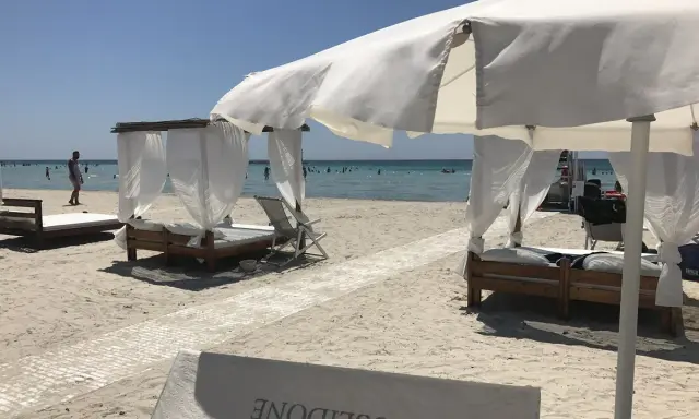 Beach cabanas with white curtains and beds on a sandy beach with the ocean in the background.