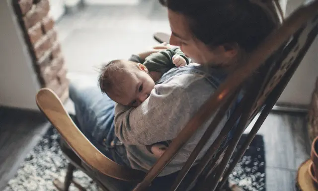 Ein Baby schläft friedlich auf dem Arm einer Person, die in einem Schaukelstuhl sitzt. Es ist, als ob die Babys im Bauch noch träumen, bevor sie die Welt entdecken.