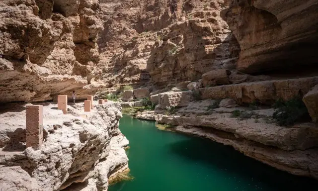 Wadi Shab w Oman: czy warto? Zielona woda w kanionie, skalne ściany i ścieżka z kamiennymi słupkami. Niesamowite widoki.