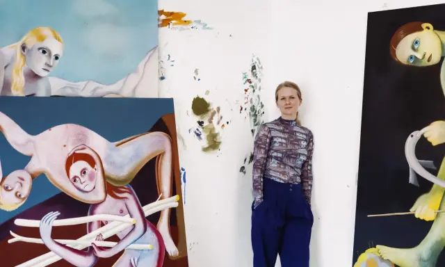 A woman stands in her studio surrounded by her surreal, figurative paintings, showcasing her as one of today's popular contemporary artists.