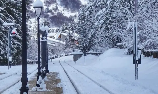Stazione innevata, binari coperti di neve, lampioni e alberi imbiancati. Un paesaggio da **campo di Giove** in inverno.