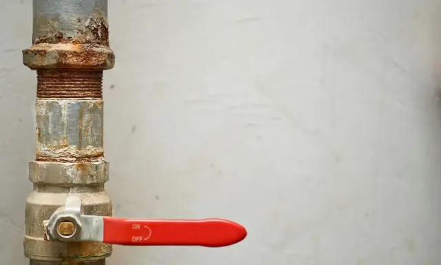 Tubería oxidada con una llave de paso general roja, lista para controlar el flujo.