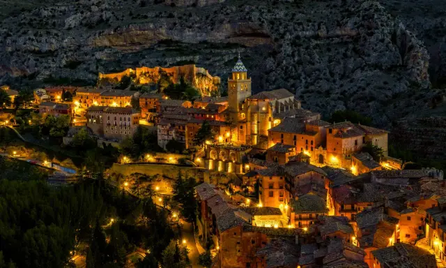 Pueblo iluminado al anochecer, ideal para planes para el puente de diciembre. Casas de piedra y tejados se asoman entre la montaña.