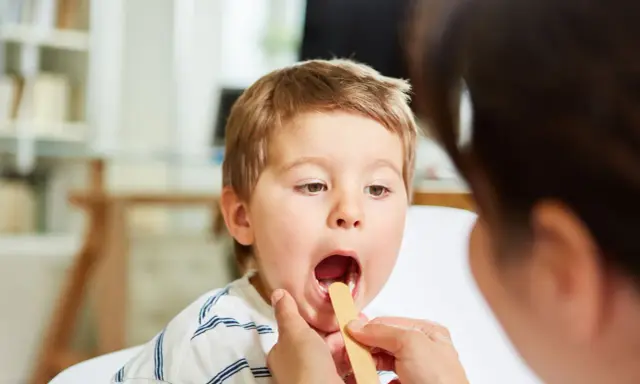 Bambino con bocca aperta durante visita medica per sospetta laringite.