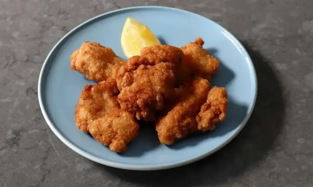 Chrupiący kurczak karaage na niebieskim talerzu, z kawałkiem cytryny.