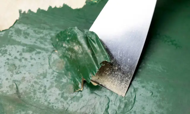 Espátula metálica retirando pintura verde descascarada de una pared. Proceso de cómo quitar pintura de la pared.