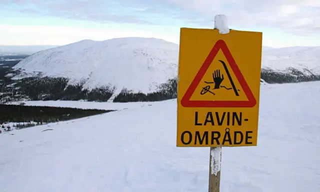 Varning för lavin vid Kebnekaise. Ett gult varningsskylt med en hand, skidor och rep i en röd triangel.