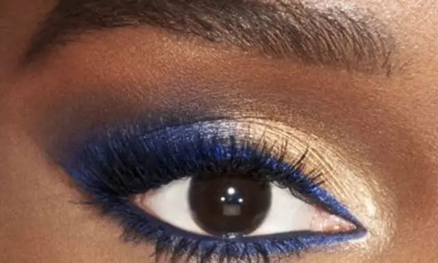 Ojo con un audaz maquillaje de ojos azul y dorado. Delineador azul vibrante y sombras doradas brillantes resaltan la mirada.