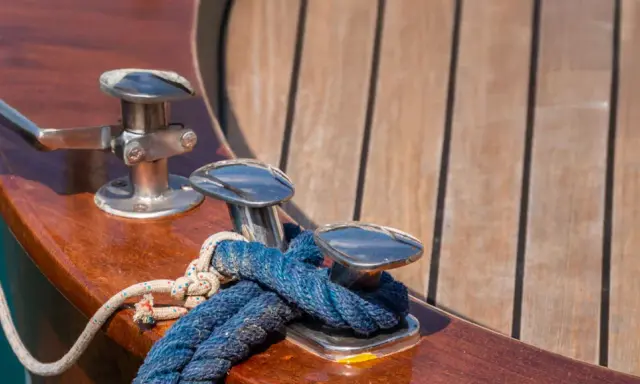 Corde bleue et blanche nouée sur des taquets chromés, prêts pour nettoyer le pont du bateau. Le bois verni brille au soleil.