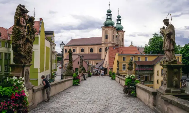 Kamienny most z rzeźbami i barokową architekturą, w tym kościołem z zielonymi kopułami. To piękne ziemia kłodzka atrakcje.