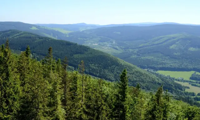 Zielone, zalesione zbocza Gór Opawskich schodzą ku dolinie z polami i zabudowaniami.