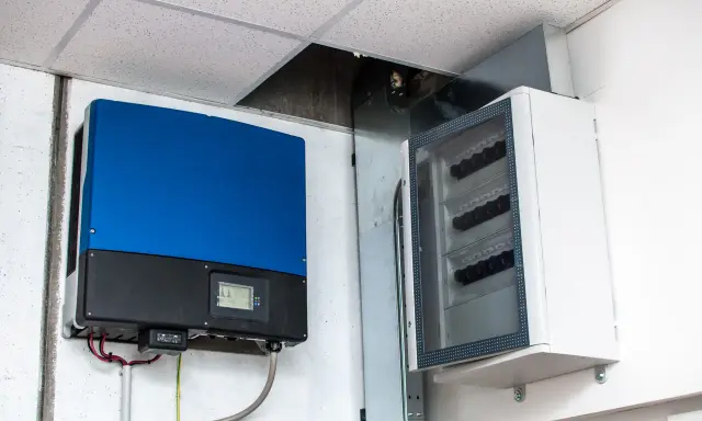 Niebieski falownik, kluczowy element instalacji fotowoltaicznej, zamontowany obok białej skrzynki z zabezpieczeniami.