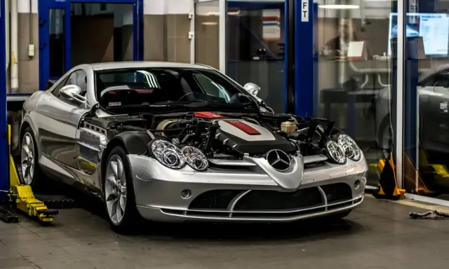Srebrny Mercedes McLaren z otwartą maską, odsłaniającą potężny silnik, stoi w warsztacie.