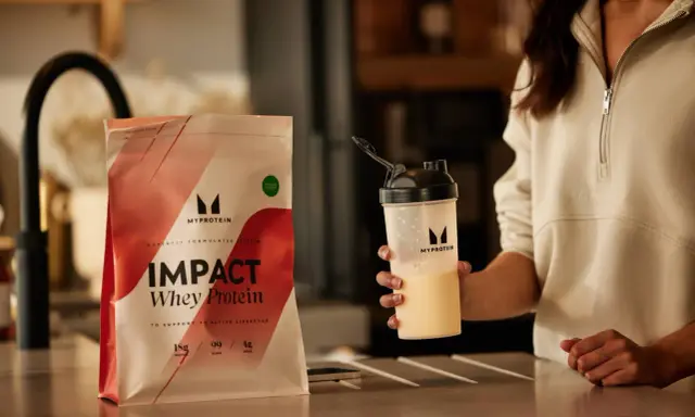 Eine Person hält einen Shaker mit einem cremigen Getränk. Daneben liegt eine Packung Myprotein Impact Whey Protein. Perfekt für den proteinshake vor dem schlafen.