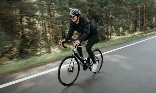 Mężczyzna w kasku i okularach jedzie na rowerze szosowym przez las. To świetny sposób, jak schudnąć na rowerze, poprawiając kondycję.