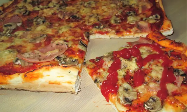 Pyszna pizza na cienkim cieście z pieczarkami i szynką, polana ketchupem. Idealna na szybki obiad.